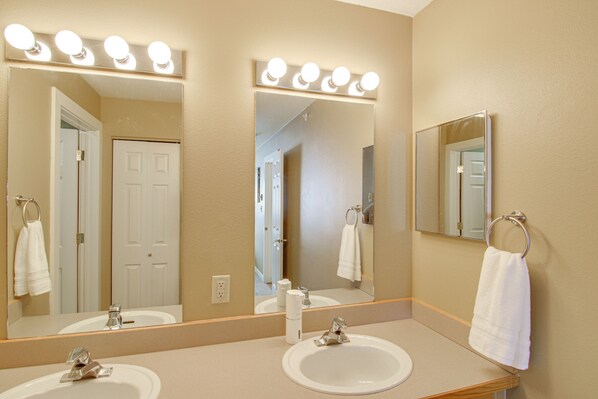 A bathroom with two sinks, a large mirror with lights, and a towel rack.