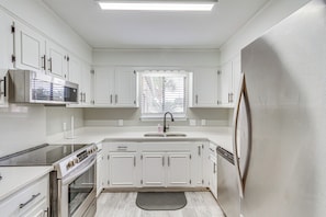 A modern kitchen with white cabinetry, a stainless steel microwave, a built-in oven, and a refrigerator. - Pensacola Home w/ Screened Porch: 10 Mi to Beach! (Pensacola)