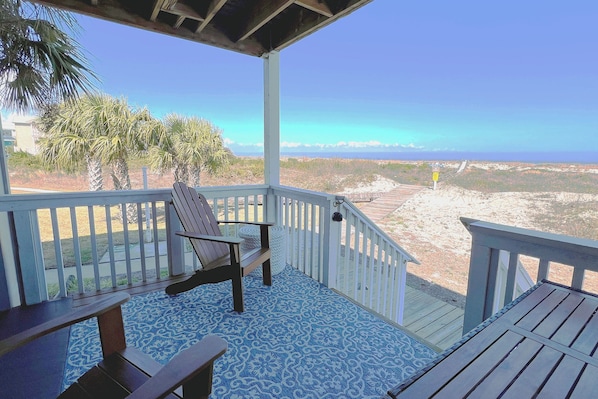 A covered outdoor area with a view of the beach, a wooden chair, and a table.