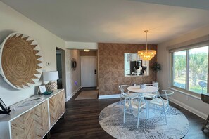 A modern kitchen with a dining area, large windows, and a decorative wall piece.