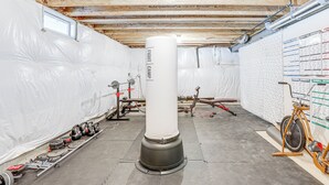 A basement with insulation, a large white pillar, gym equipment, and a wall with workout charts. - Spacious Ewing Township Home: Home Gym & Deck! (Trenton)