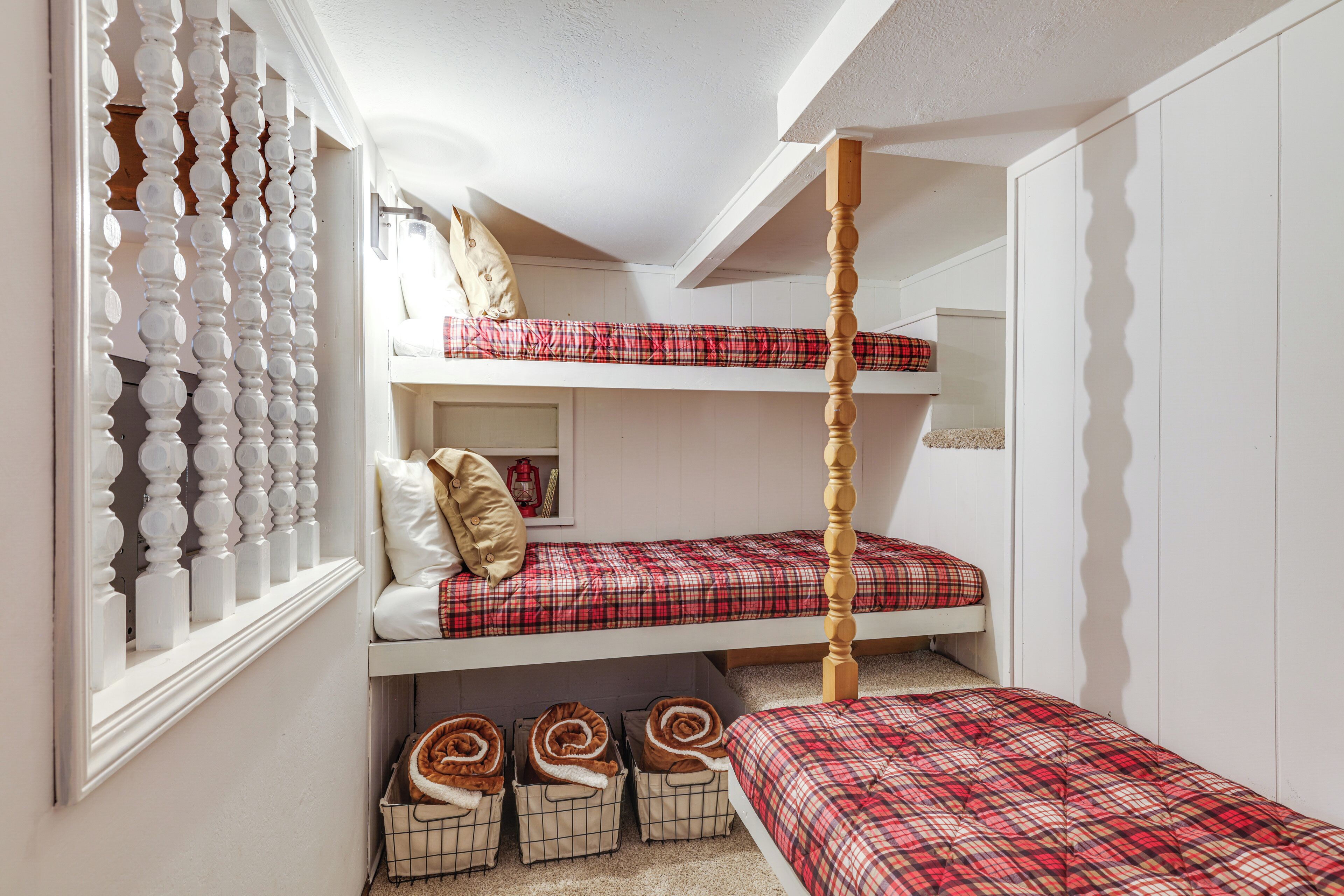 Habitació amb un llit superposat, una escala de fusta, una finestra amb una reixa decorativa i calaixos sota el llit.