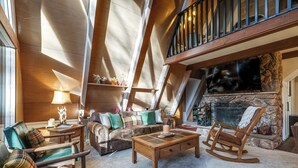 A cozy loft-style living room with a fireplace, wooden furniture, and a high ceiling with exposed beams. - 3 Mi to Calaveras Big Trees: Cabin w/ Fire Pit! (Arnold)