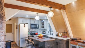 A modern kitchen with wooden beams, a central island, and a stone wall. - 3 Mi to Calaveras Big Trees: Cabin w/ Fire Pit! (Arnold)