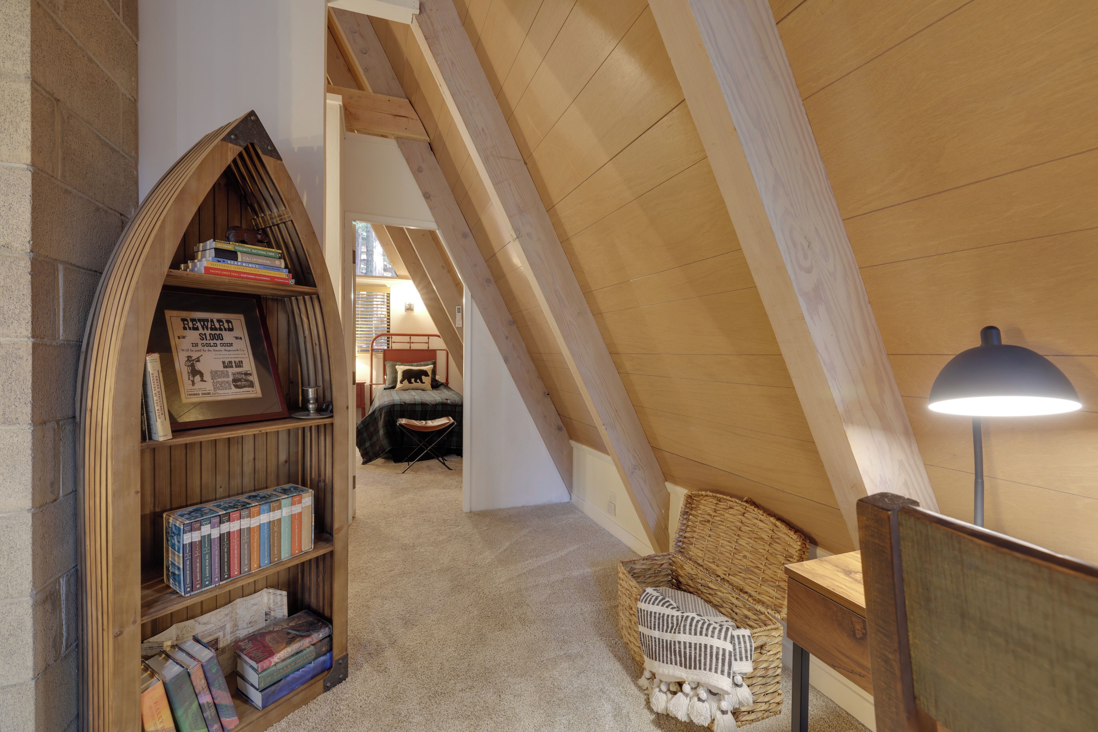 A cozy attic room with a wooden bookshelf, a wicker chair, and a lamp.