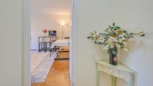 Et værelse med et spisebord og stole, et lille bord med en vase blomster, og en lampe i baggrunden.