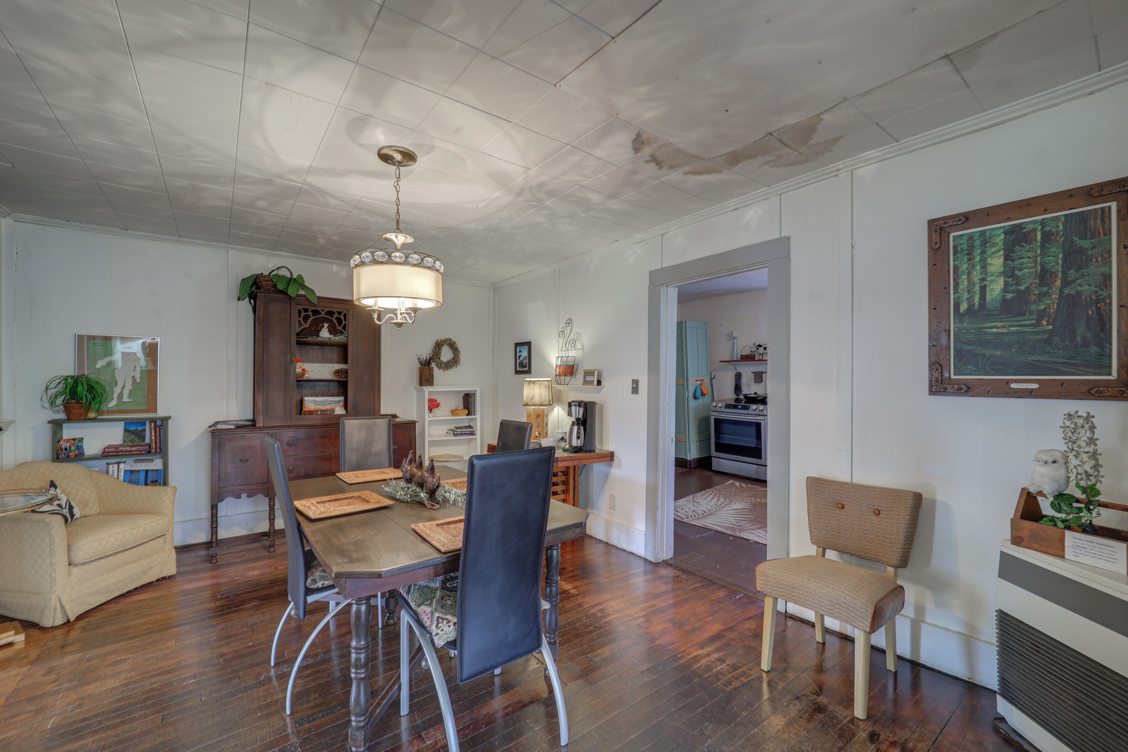 Un ampio soggiorno con un tavolo da pranzo in legno, sedie e un lampadario. C'è un divano, una libreria e un quadro appeso al muro.