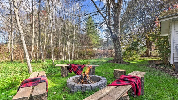 A backyard with a fire pit, wooden benches, and a house in the background. - Mtn Cottage w/ Fire Pit in Newland! (Newland)