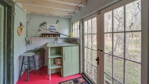 A room with a green desk, a chair, a window with a view of trees, and a door. - Mtn Cottage w/ Fire Pit in Newland! (Newland)