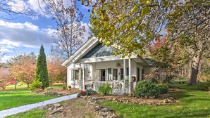 A single-story house with a porch, surrounded by a well-maintained lawn and trees. - Mtn Cottage w/ Fire Pit in Newland! (Newland)
