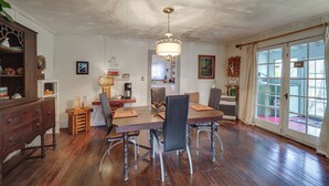 A dining area with a wooden table, chairs, and a chandelier. There is a cabinet with decorative items and a view of the outside through a glass door. - Mtn Cottage w/ Fire Pit in Newland! (Newland)