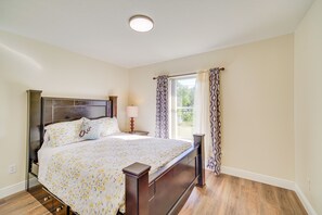 A bedroom with a wooden bed, a nightstand, a lamp, and a window with curtains.