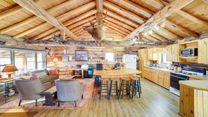 A rustic cabin interior with a dining area, kitchen, and a ceiling-mounted animal head. - Yellowstone Cabin Getaway Near National Park (Cameron)