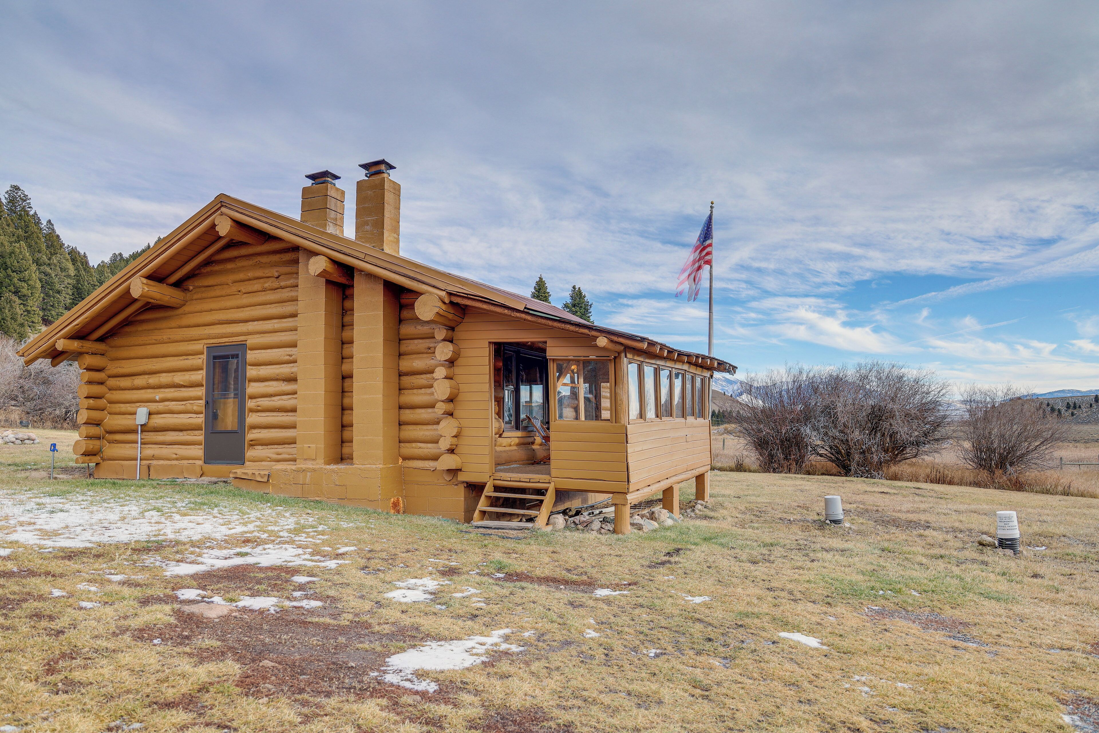 A log cabin with a porch, a chimney, and an American flag.