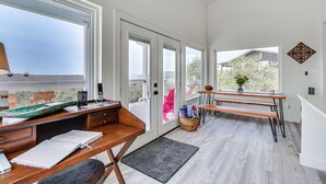 Une chambre moderne avec un bureau en bois, des livres ouverts, un ordinateur portable et une fenêtre donnant sur un balcon.