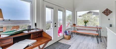 A modern room with a wooden desk, open books, a laptop, and a window overlooking a balcony.