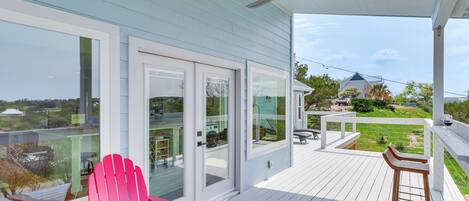 A covered deck with a ceiling fan, a red Adirondack chair, and a white table.