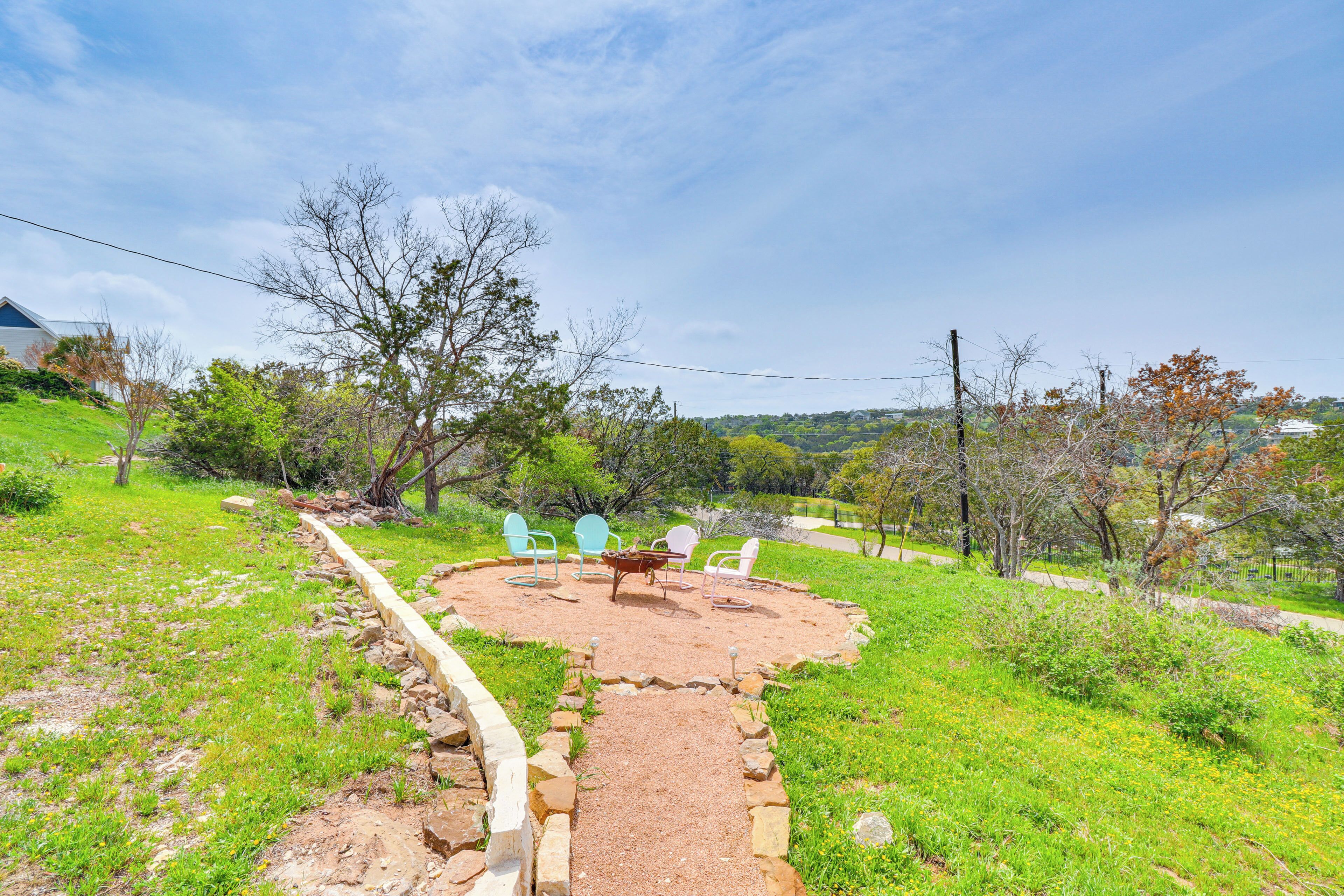 A circular outdoor seating area with a fire pit, surrounded by a stone border and a gravel path leading to it.