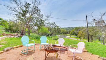 An outdoor seating area with four chairs and a round table, surrounded by a natural landscape with trees and a clear sky.