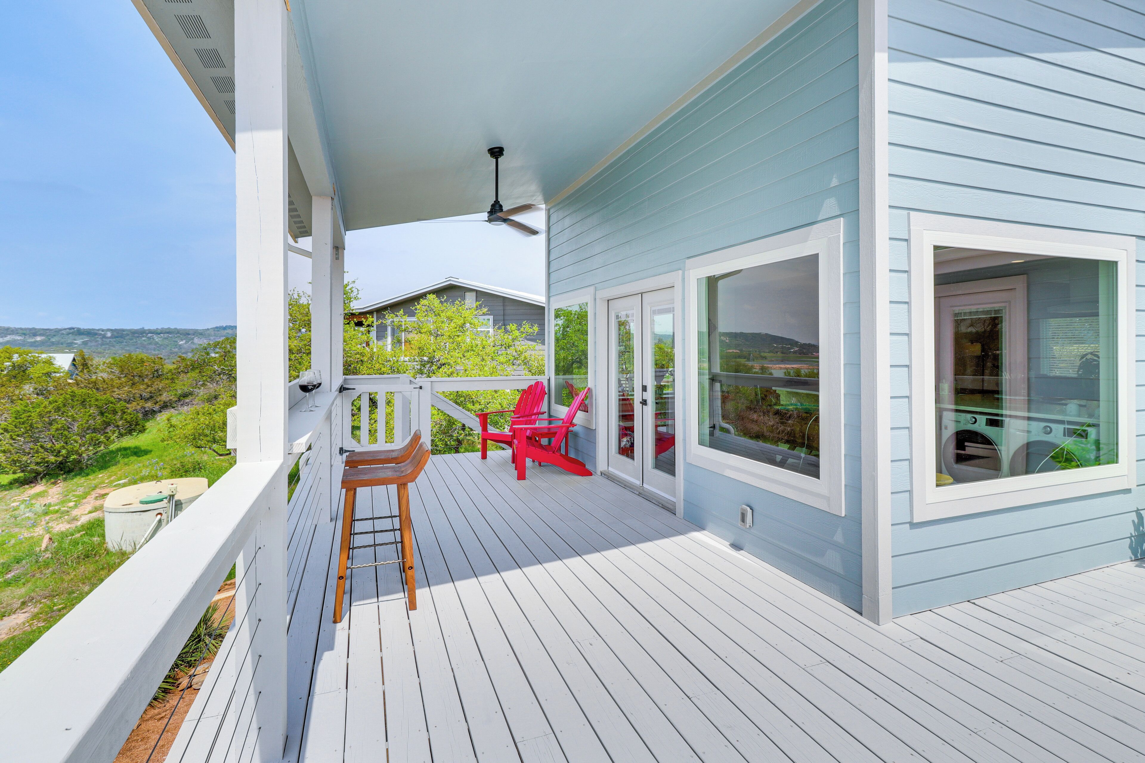 A covered deck with white railings, red Adirondack chairs, and a view of the landscape.