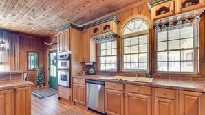 A kitchen with wooden cabinets, a dishwasher, a sink, and a window with a curtain. - Countryside Cabin Rental ~ 10 Mi to Wadesboro! (Wadesboro)
