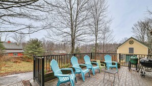 Een terras met vier Adirondack-stoelen, een barbecue en een kleine schuur.