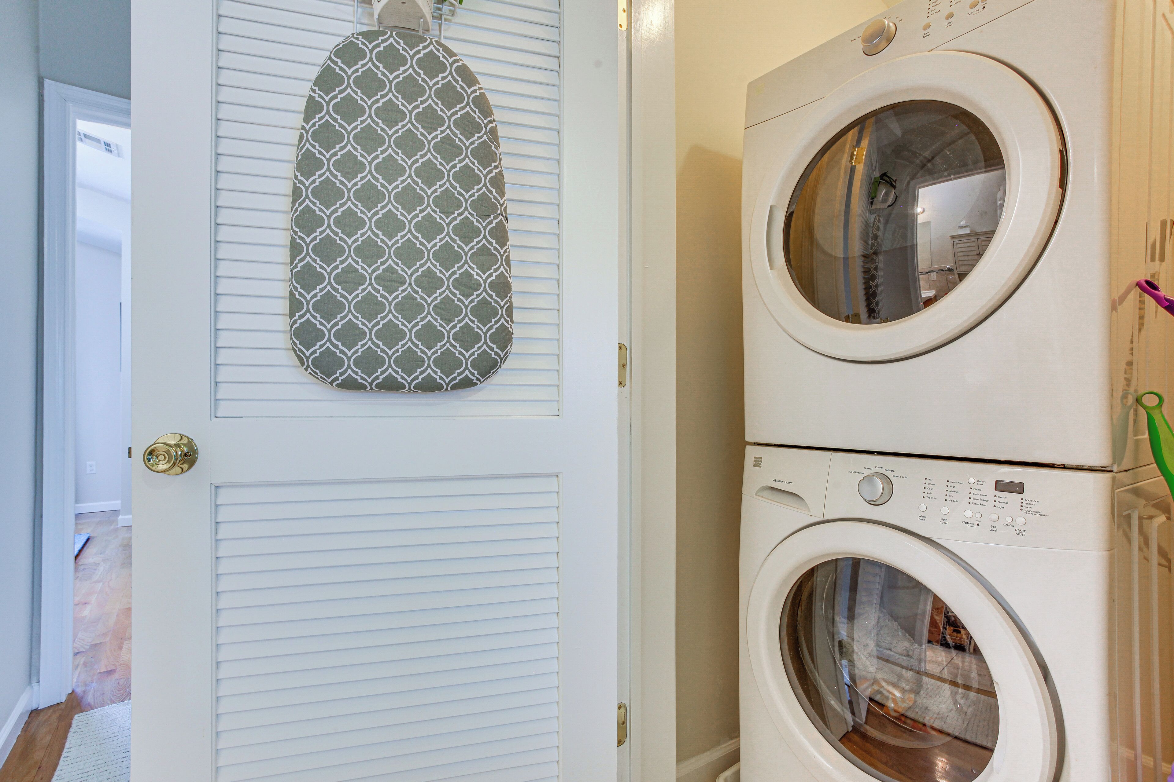Une buanderie équipée d’un lave-linge et d’un sèche-linge superposés, une serviette à motifs accrochée à la porte et une poignée de porte bien visible.