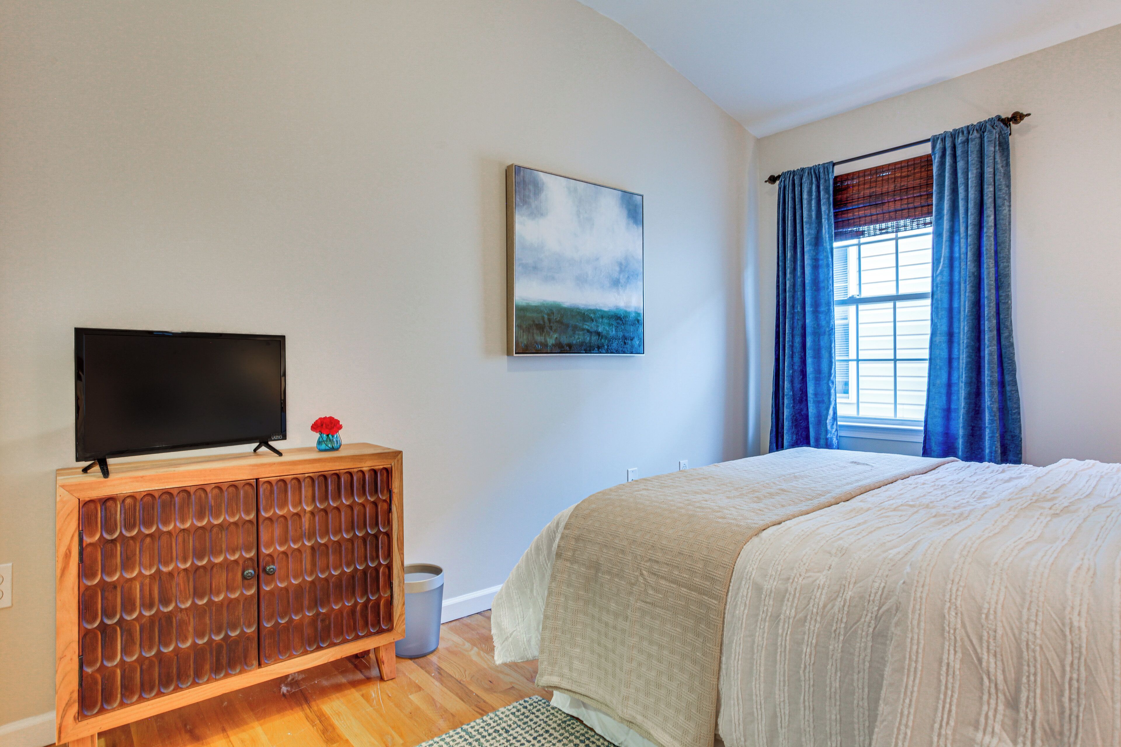 Una camera da letto con un letto, una TV su un mobile in legno, un quadro appeso al muro e una finestra con tende.