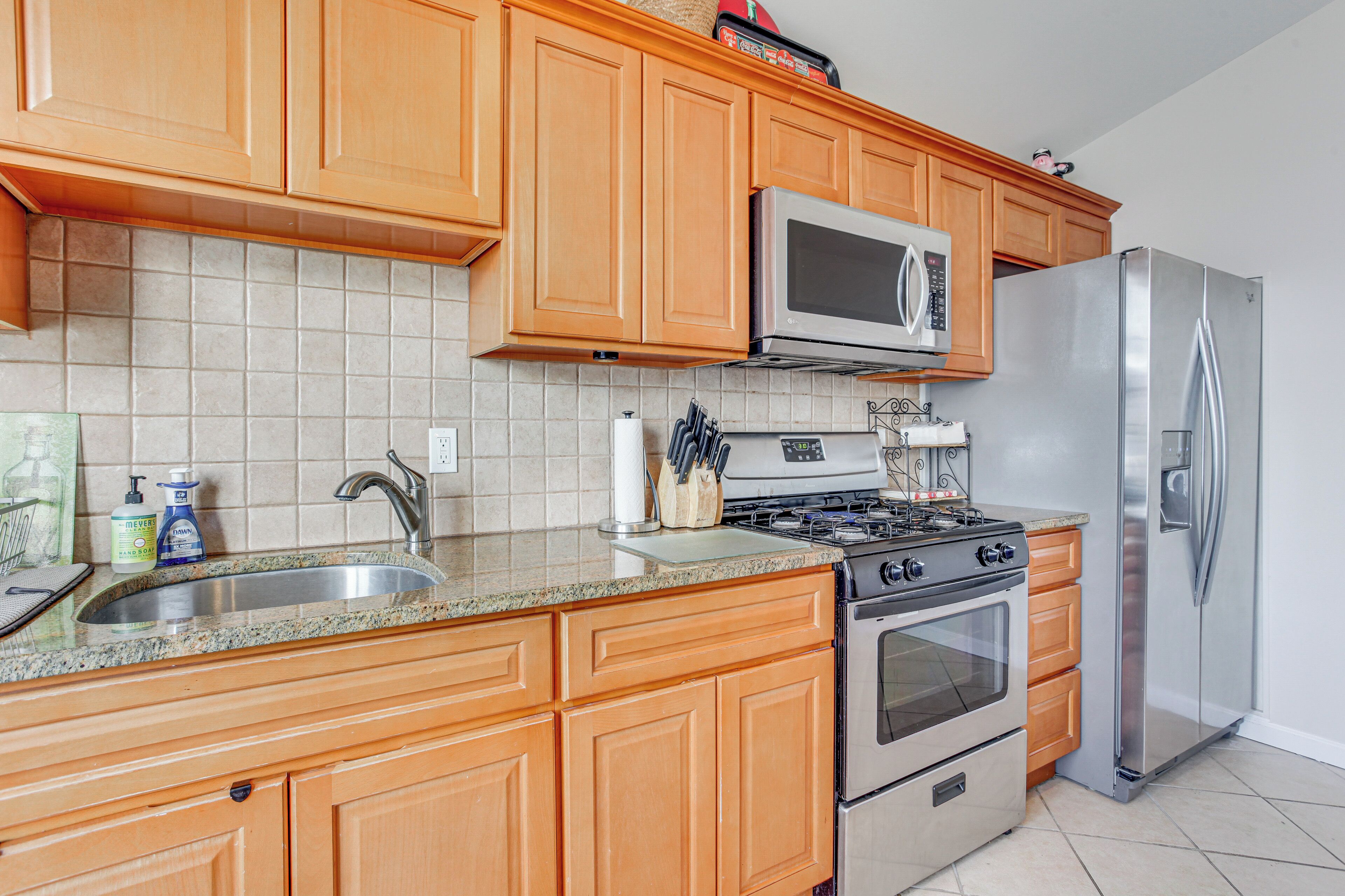 A kitchen with wooden cabinets, a stainless steel refrigerator, a microwave, and a gas stove.