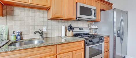 A kitchen with wooden cabinets, a stainless steel refrigerator, a microwave, and a gas stove.