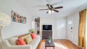 Un salon avec un canapé blanc, une table basse en bois foncé, un ventilateur de plafond, un téléviseur et un tapis à motifs.