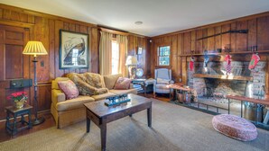 A cozy living room with wooden paneling, a fireplace, a sofa, a coffee table, and a lamp. - Elegant Paris Manor w/ Private Pool! (Paris)