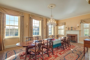 Une salle à manger avec une grande table, des chaises, un lustre et une cheminée.