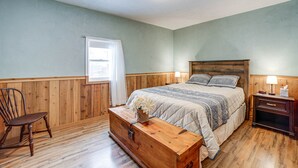 Quarto com cabeceira de madeira, cômoda de madeira, cadeira de balanço de madeira e mesa de cabeceira com abajur.