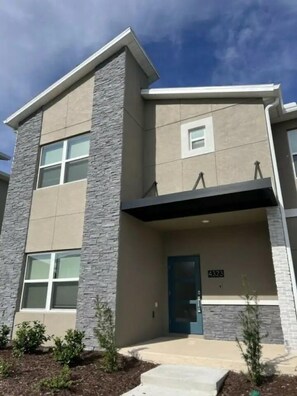 A modern two-story building with a stone facade, a blue door, and a small porch area. - 4323sl-storey Lake Resort 5 Bedroom Townhouse by RedAwning (Kissimmee)