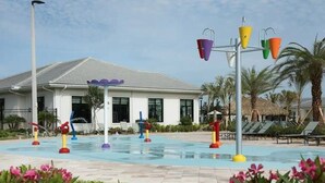 Un área de piscina con coloridas fuentes de agua y un edificio de fachada blanca y techo gris.