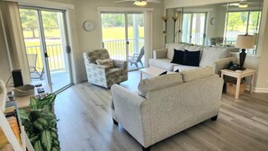 A spacious living room with a sofa, armchair, and a small table. There is a ceiling fan, a large window, and a view of a balcony. - 2804 2 Bedroom Villa by RedAwning (Calabash)