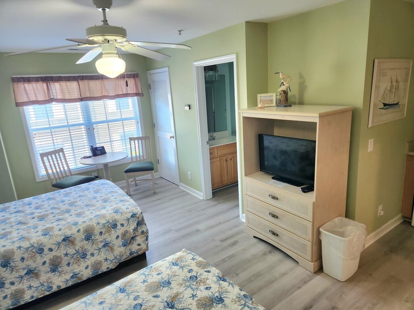 Ein Zimmer mit zwei Betten, einem Fernseher, einem Deckenventilator, einem Essbereich und einem Badezimmer.