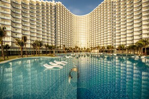 A large hotel with a curved facade, a central swimming pool, and palm trees around the pool area. - The Western Seaview Cam Ranh Condotel (Bac Cam Ranh)