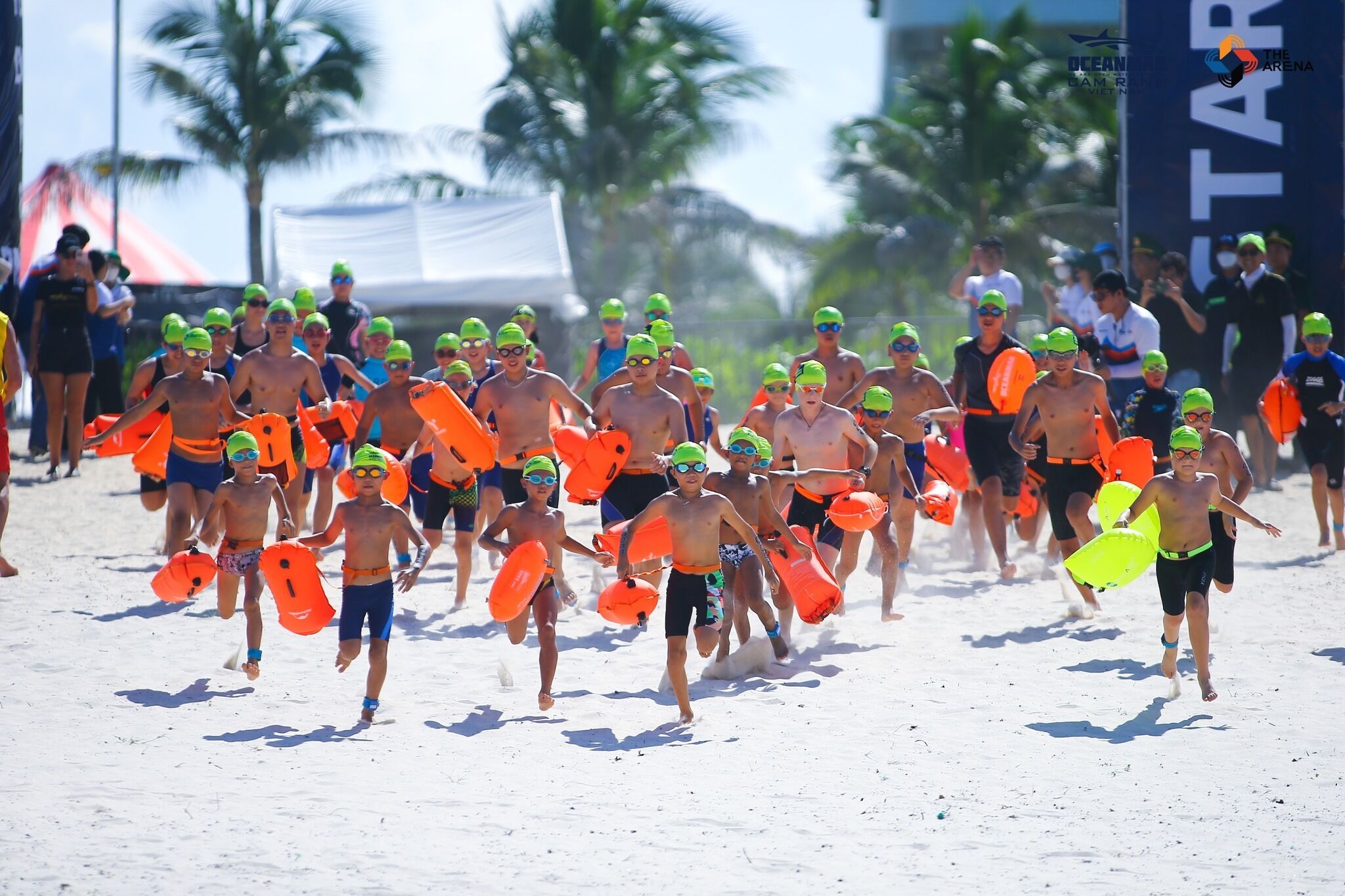 A group of people running on a beach with orange flotation devices.