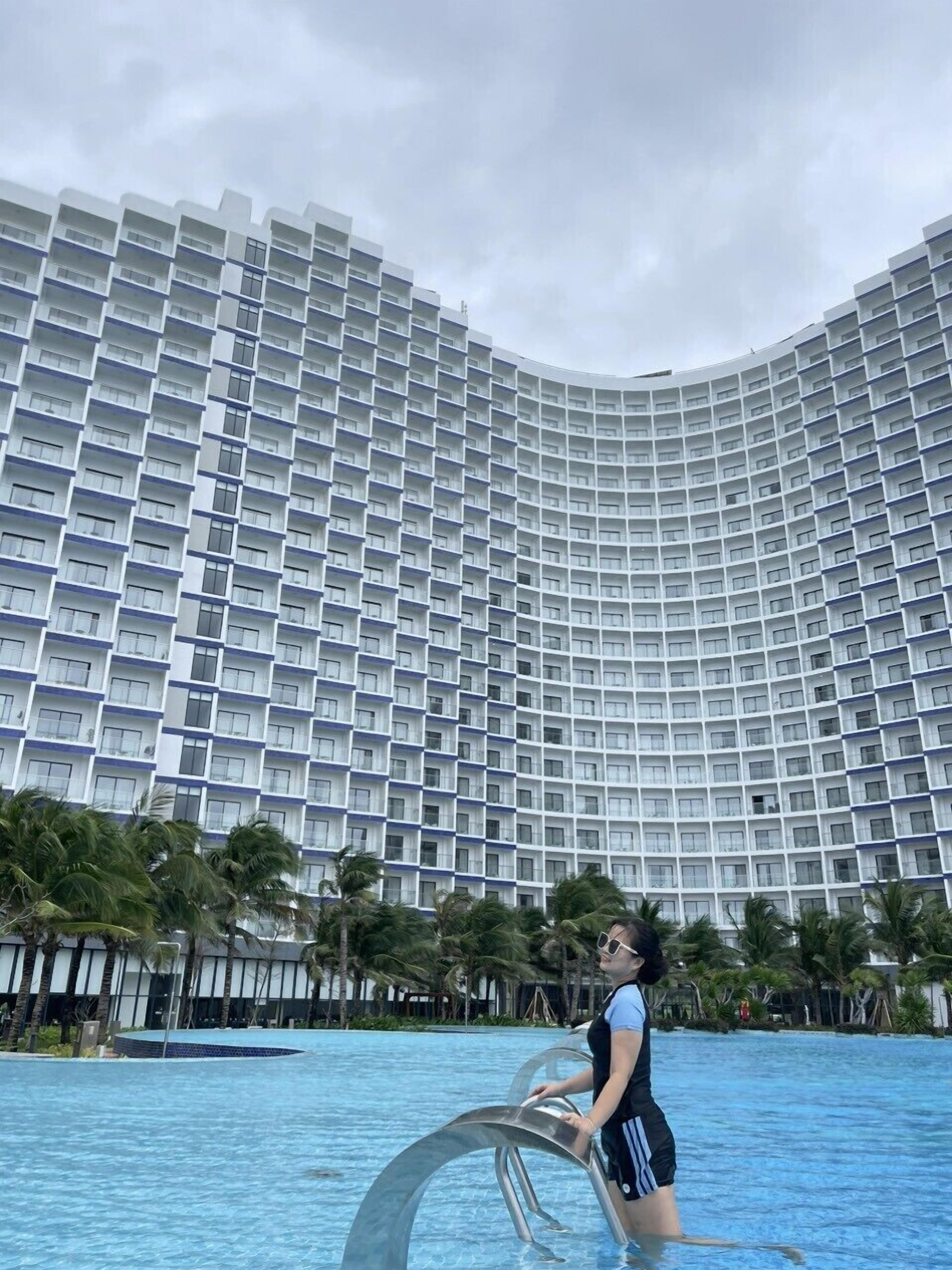 A high-rise hotel with a curved facade, a swimming pool, and palm trees.