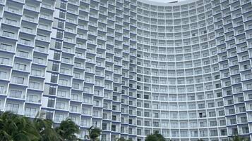 A high-rise hotel with a curved facade, a swimming pool, and palm trees.