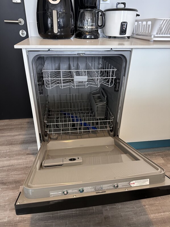 A kitchen with a dishwasher, a coffee maker, and a white pot on the counter.