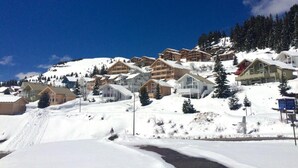 Ein schneebedecktes Bergresort mit Chalets, eine Skipiste und ein klarer, blauer Himmel.