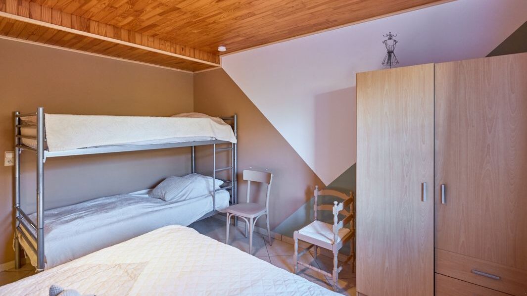 A dormitory room with bunk beds, a wooden wardrobe, and a chair.