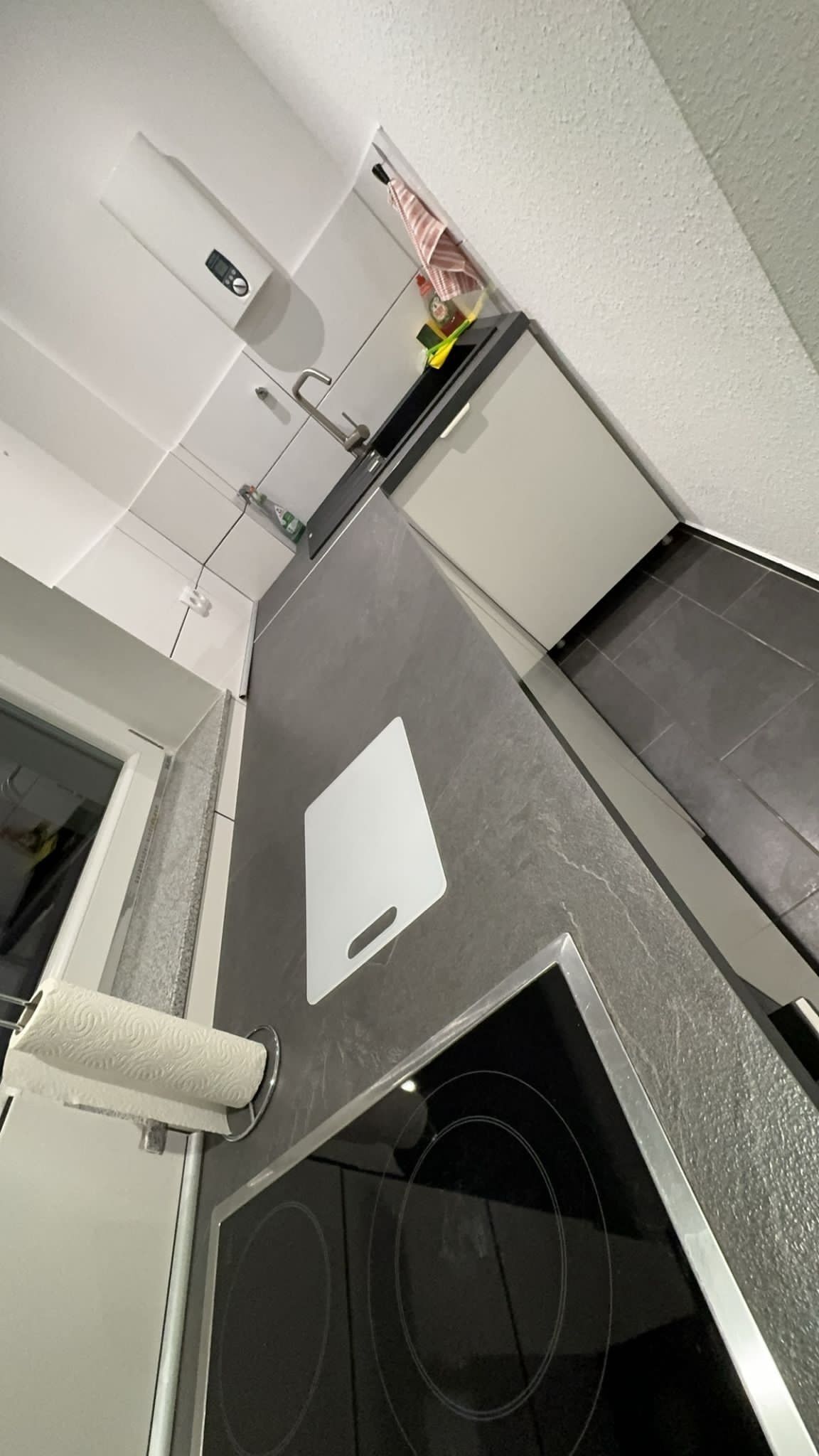 A kitchen with a black countertop, a white cutting board, a paper towel holder, and a stove.