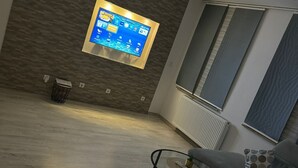 Una sala de estar moderna con un televisor de pantalla plana montado en una pared con textura, un sofá gris, una mesa de centro con una decoración de piña y un radiador.