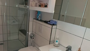 Un baño moderno con ducha de vidrio, un lavabo blanco con encimera de mármol y un espejo grande sobre el mueble.