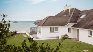 A coastal house with a sloped roof, a small deck, and a view of the sea. - Tregirls - Polzeath -  ocean view, cliff top property sleeping 10 (Polzeath)
