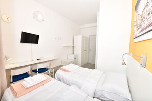 Een hotelkamer met twee bedden, een bureau met een computer, een televisie en een badkamer met een oranje wand.